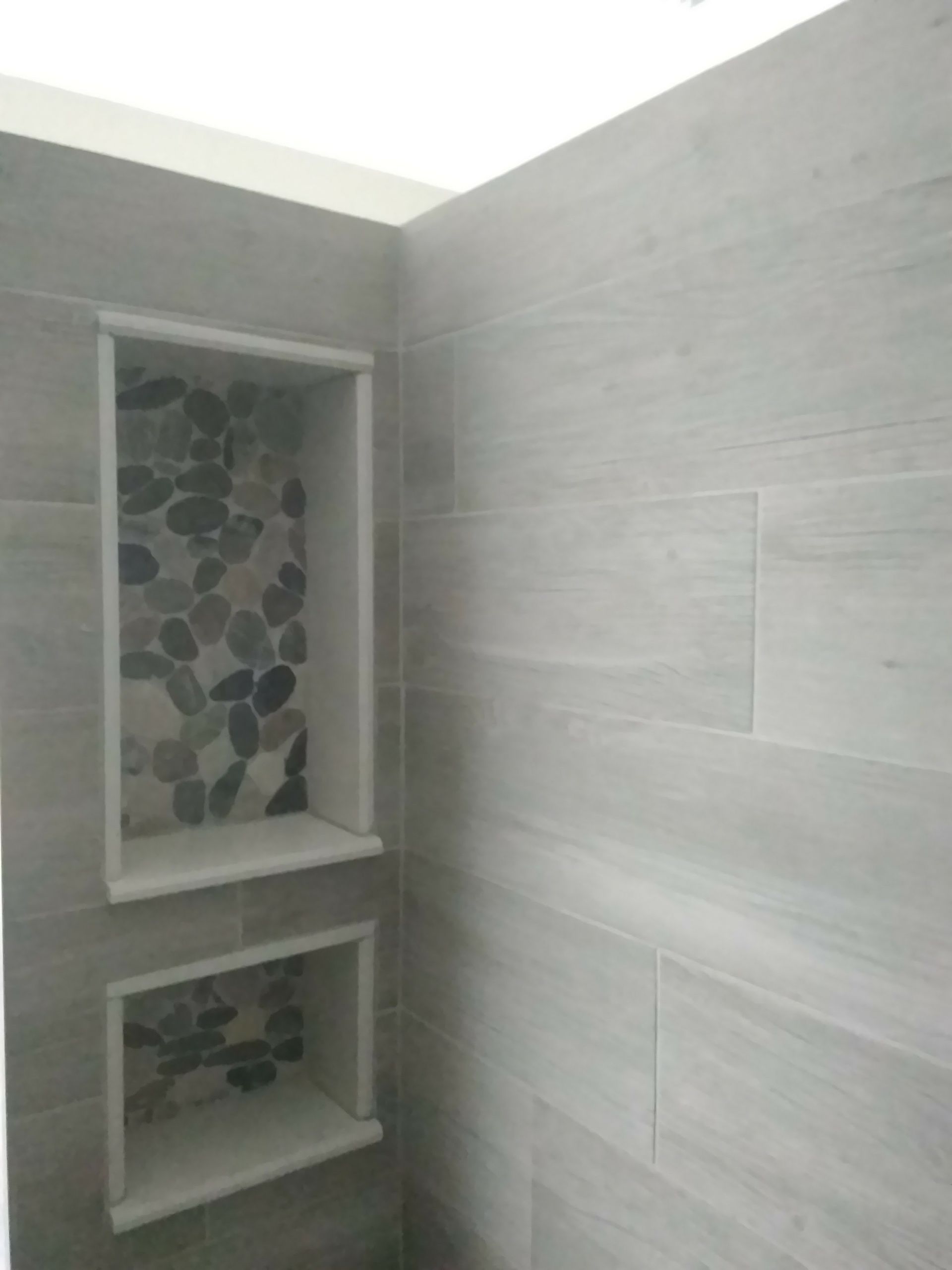 A bathroom with a stone wall and two shelves in the corner.