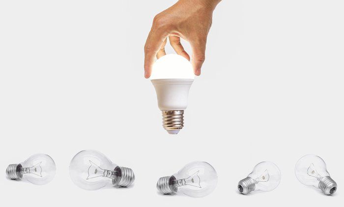 hand holding lit up light bulb and light bulbs on ground