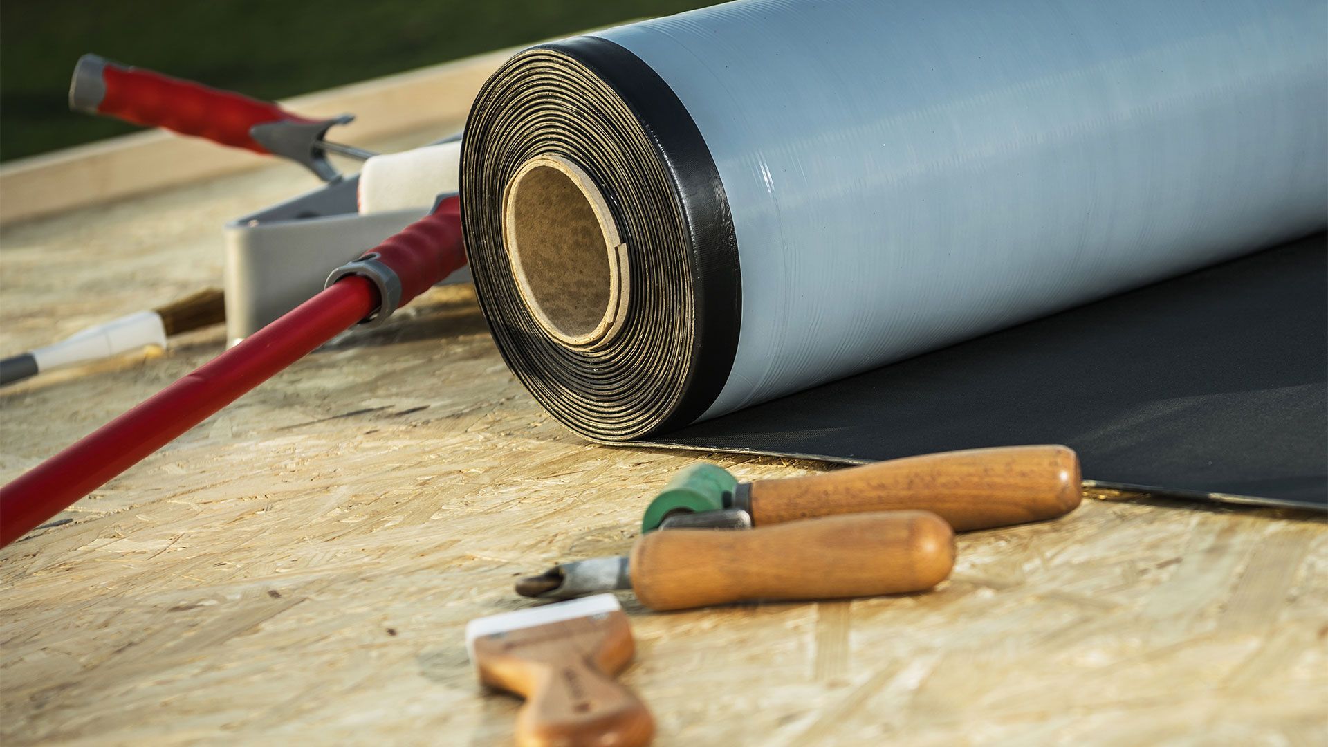 A roll of roofing material and tools on a wooden table.