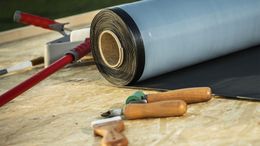 A roll of roofing material and tools on a wooden table.