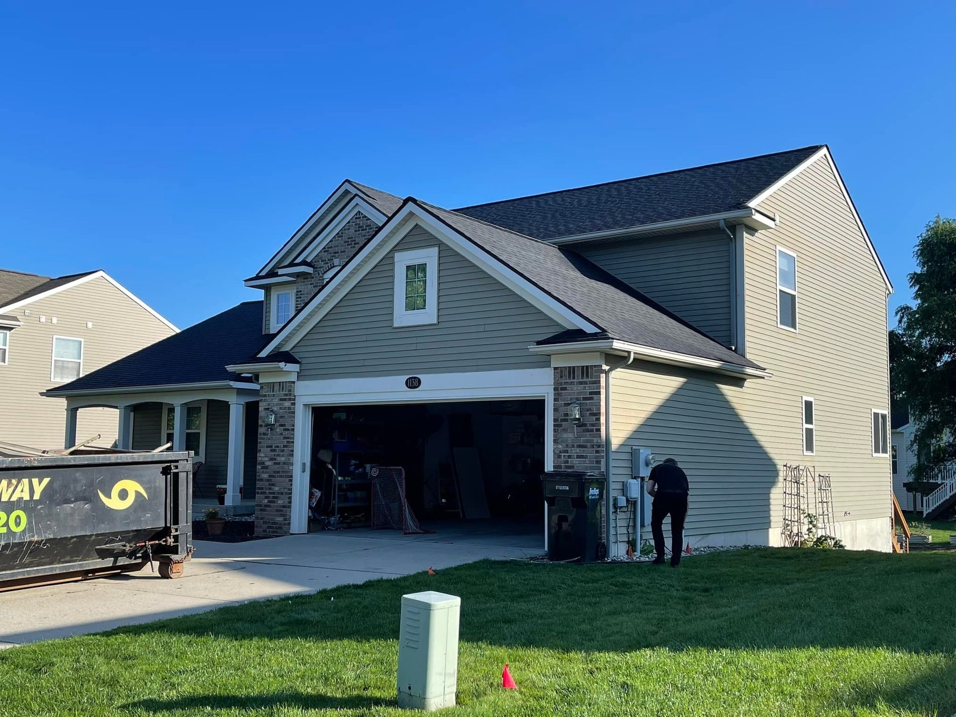 A large house with a black roof and a dumpster in front of it.