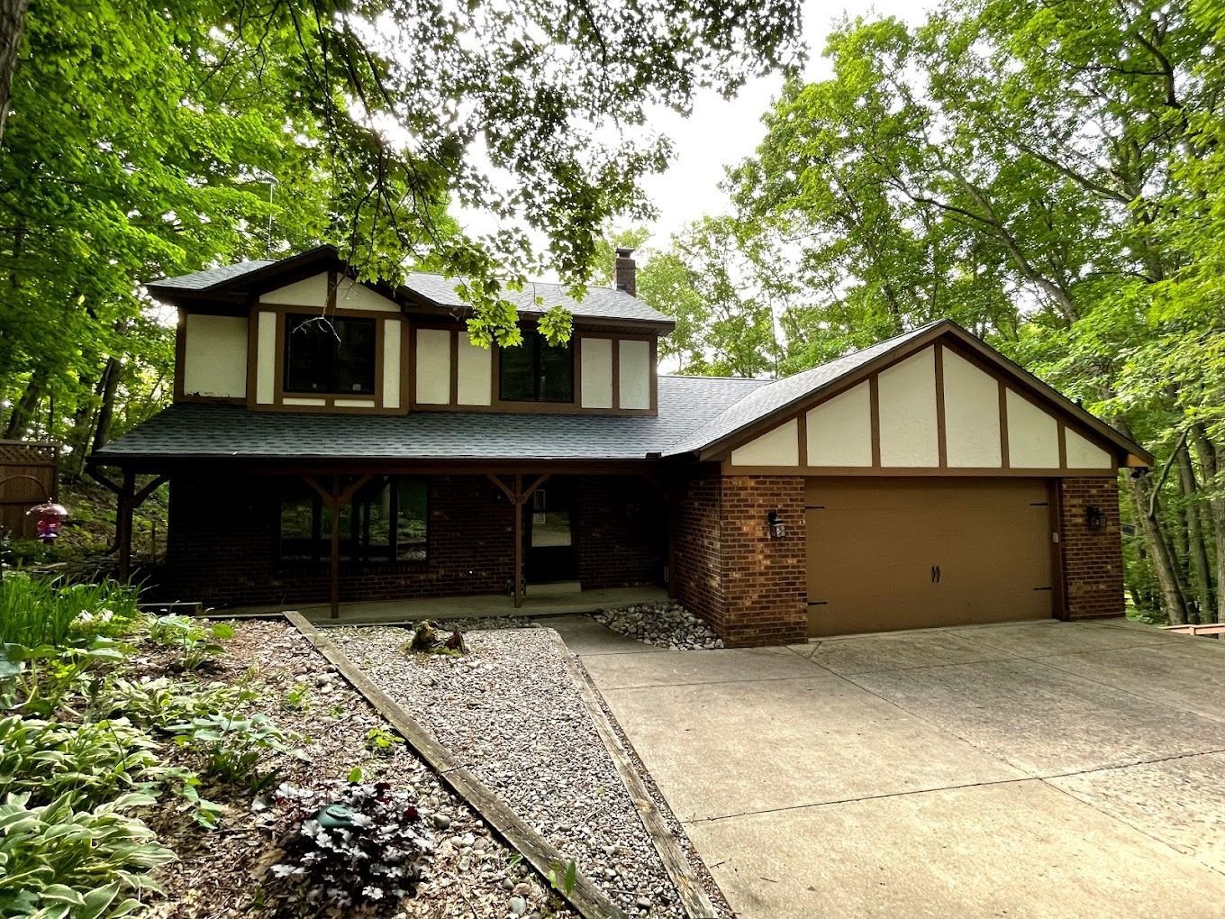 A large brick house with a garage is surrounded by trees.