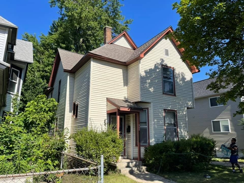 A white house with a red roof is surrounded by trees and bushes.