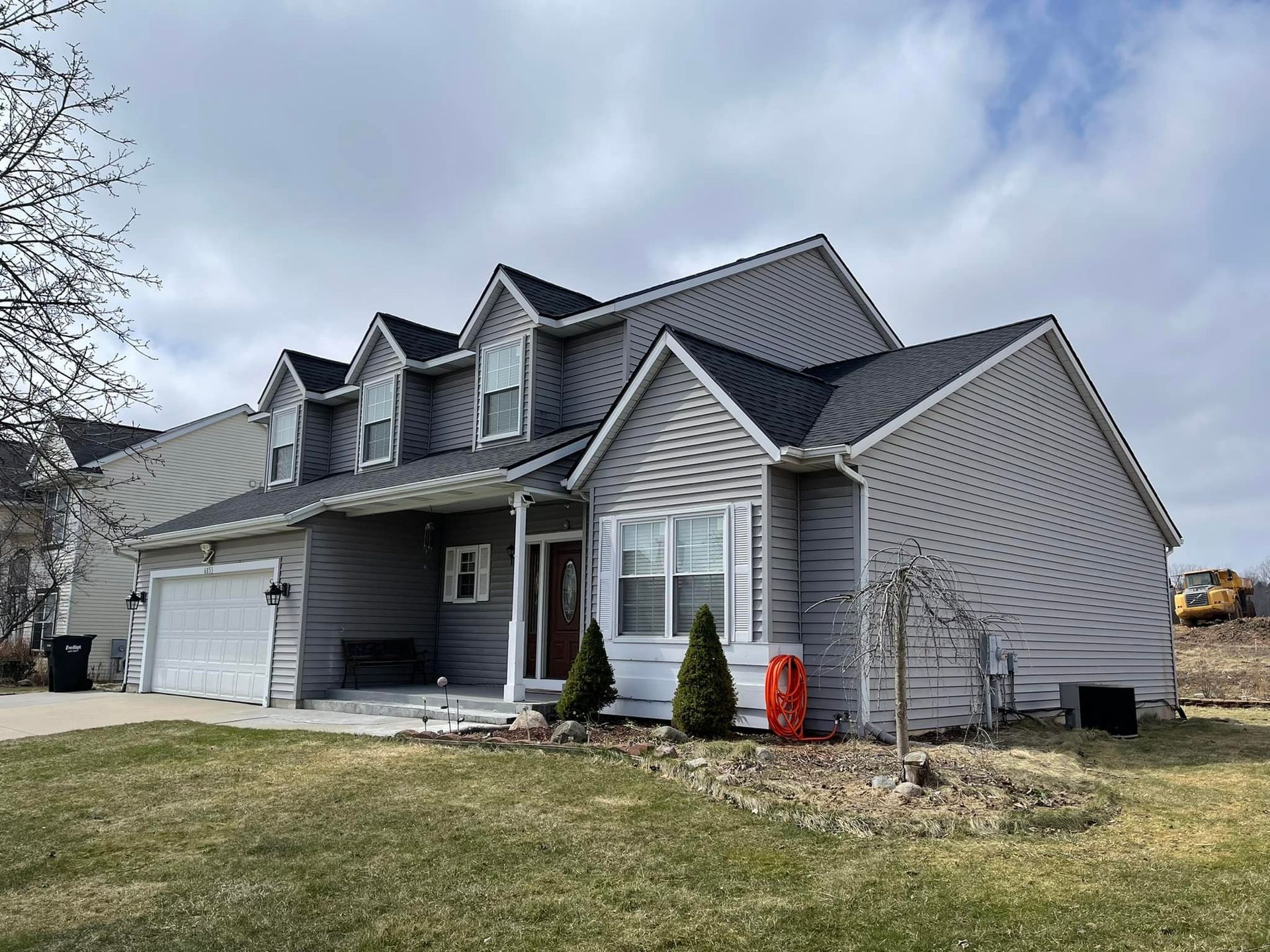 A large gray house with a black roof is sitting on top of a lush green field.