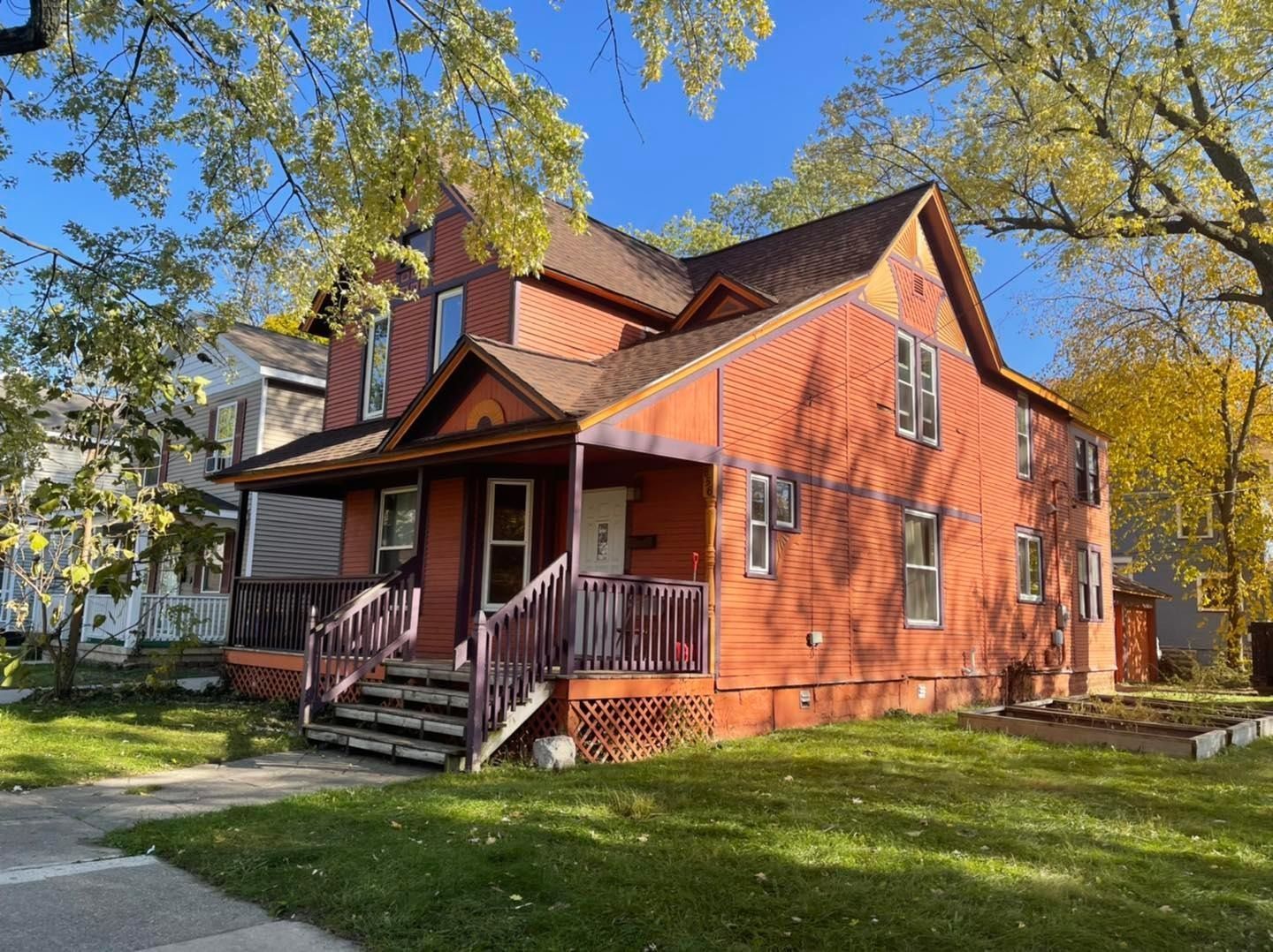 A large orange house with a porch and stairs is sitting on top of a lush green lawn.