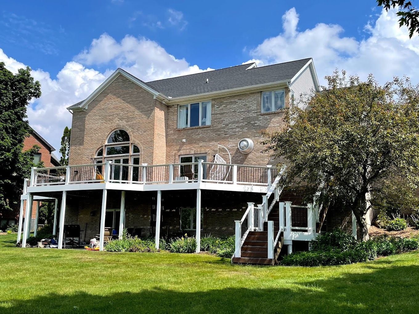 A large house with a large deck is sitting on top of a lush green field.