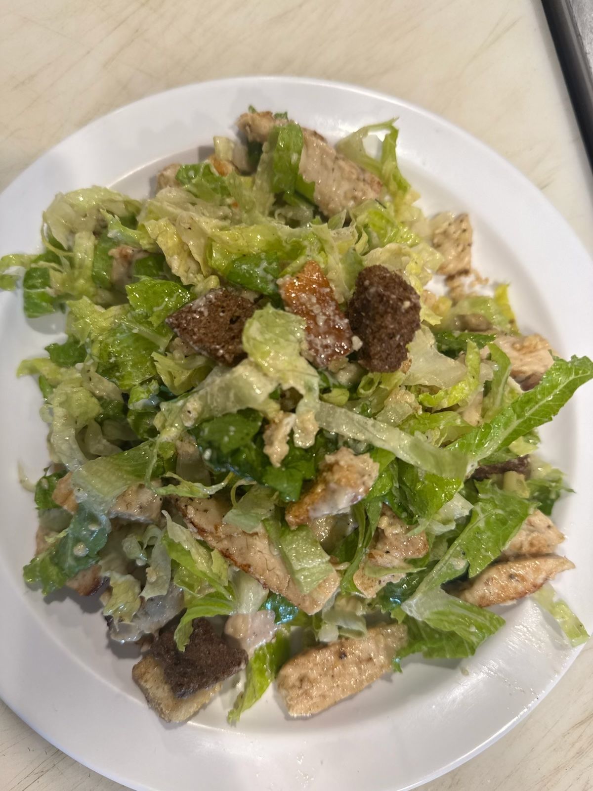 Caesar salad with chicken and croutons on a white plate.