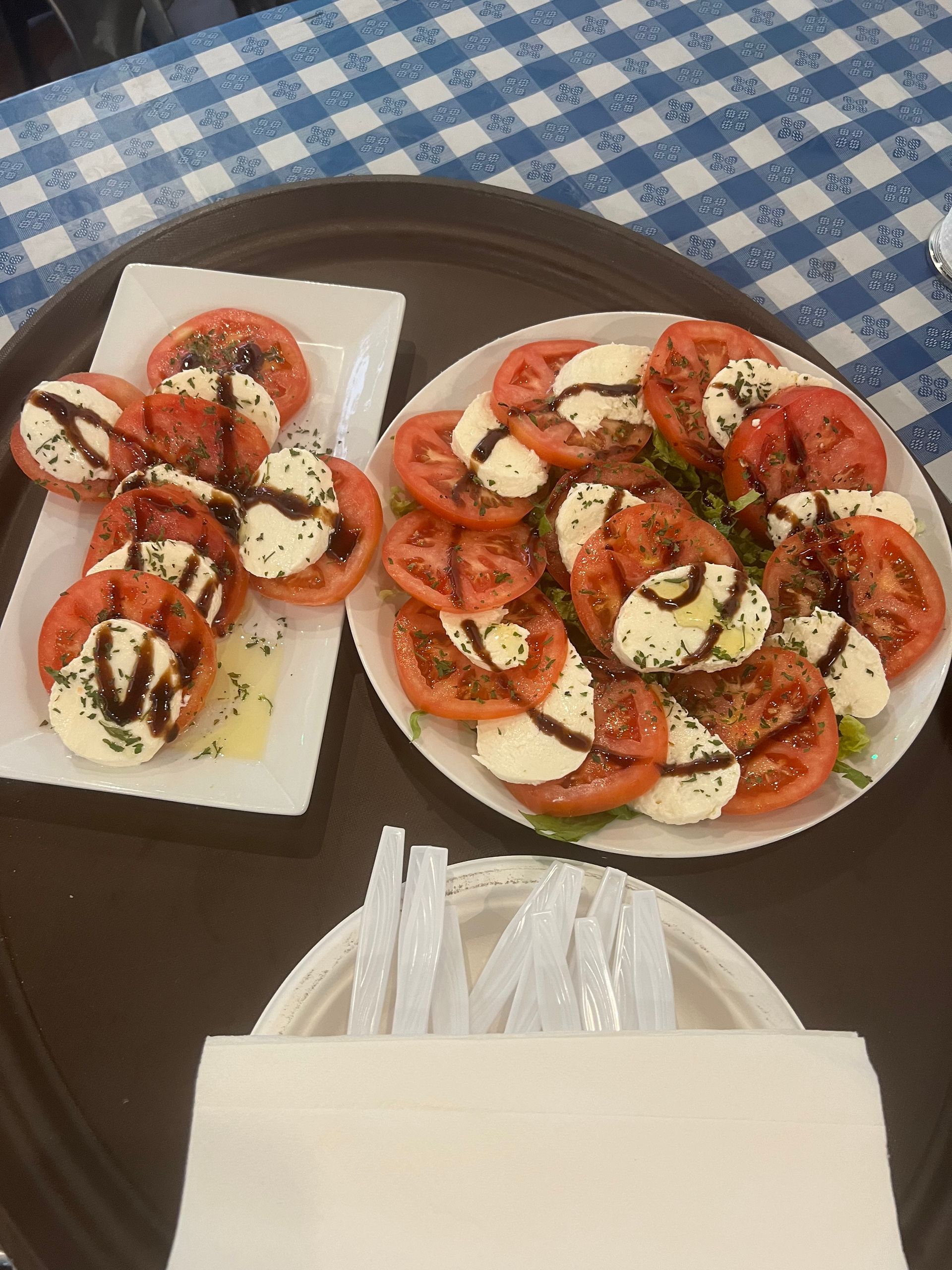 Caprese salad on a tray with tomatoes, mozzarella, balsamic glaze, and a napkin.