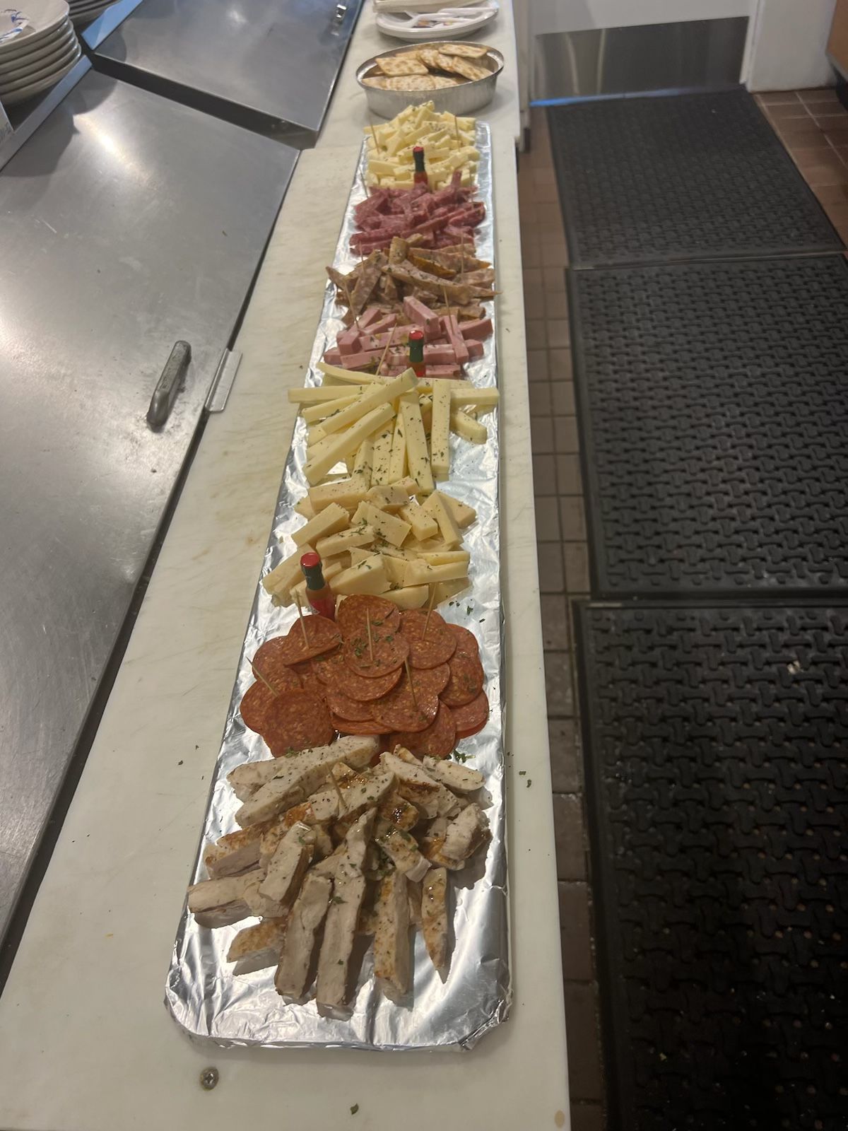A long platter of various meats and cheeses arranged in rows on a counter.