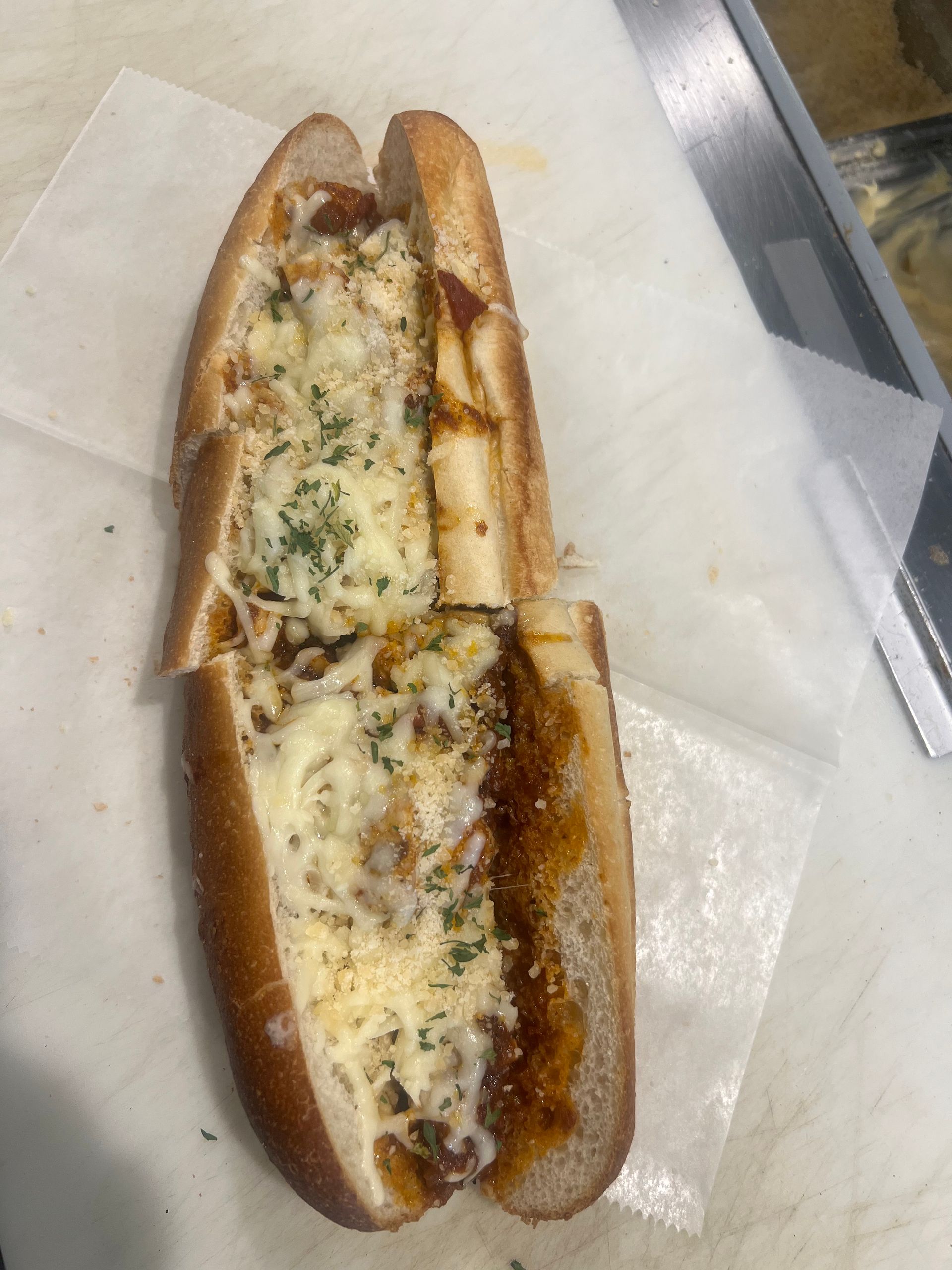 Meatball sub on a long roll, cut in half, covered in cheese and sauce, on white paper.