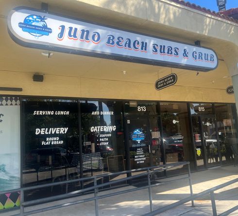 Juno Beach Subs & Grub storefront with sign, black windows, and delivery/catering notices.
