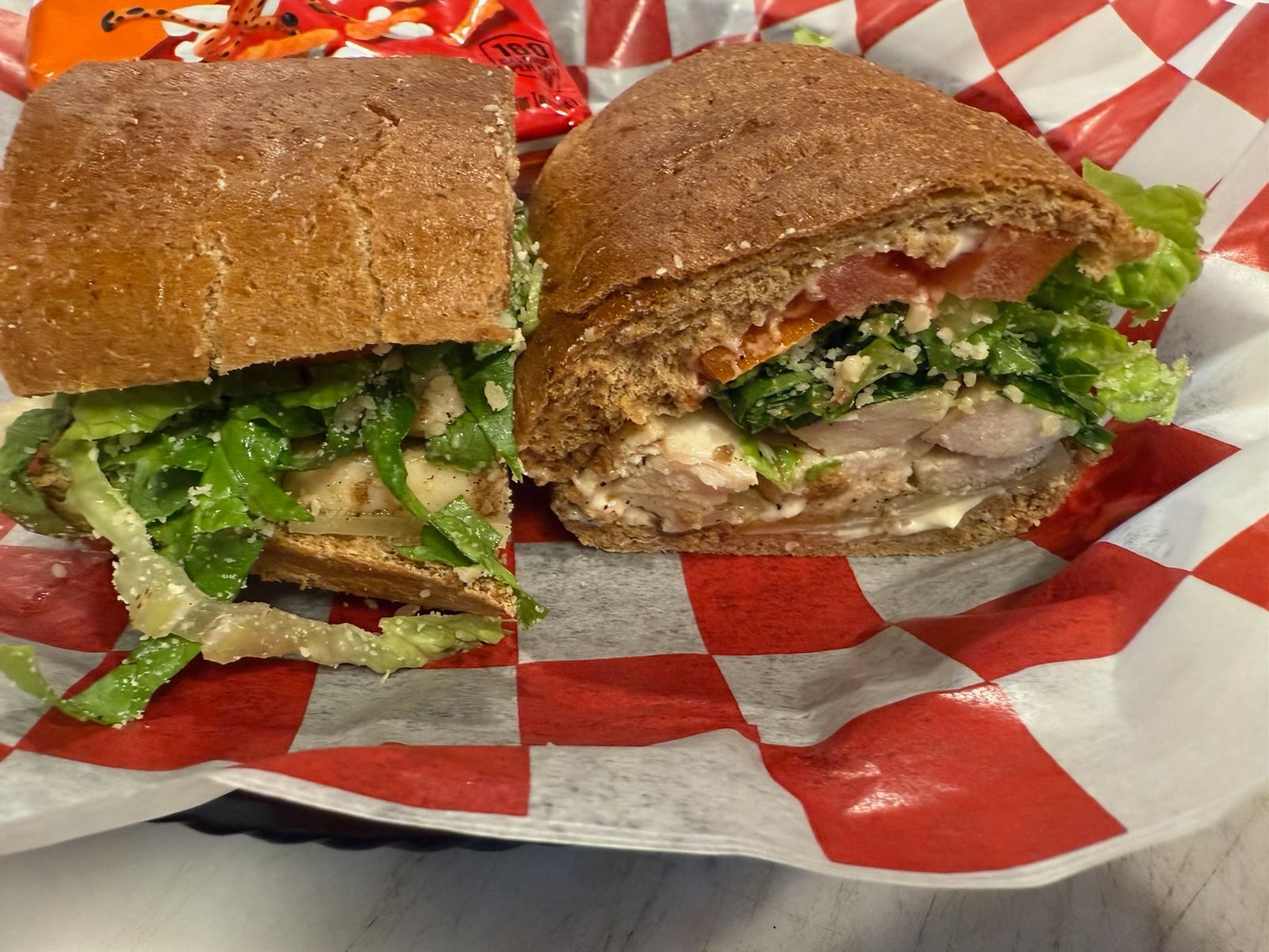 A sandwich on a checkered paper, cut in half. Contains meat, lettuce, and tomato.