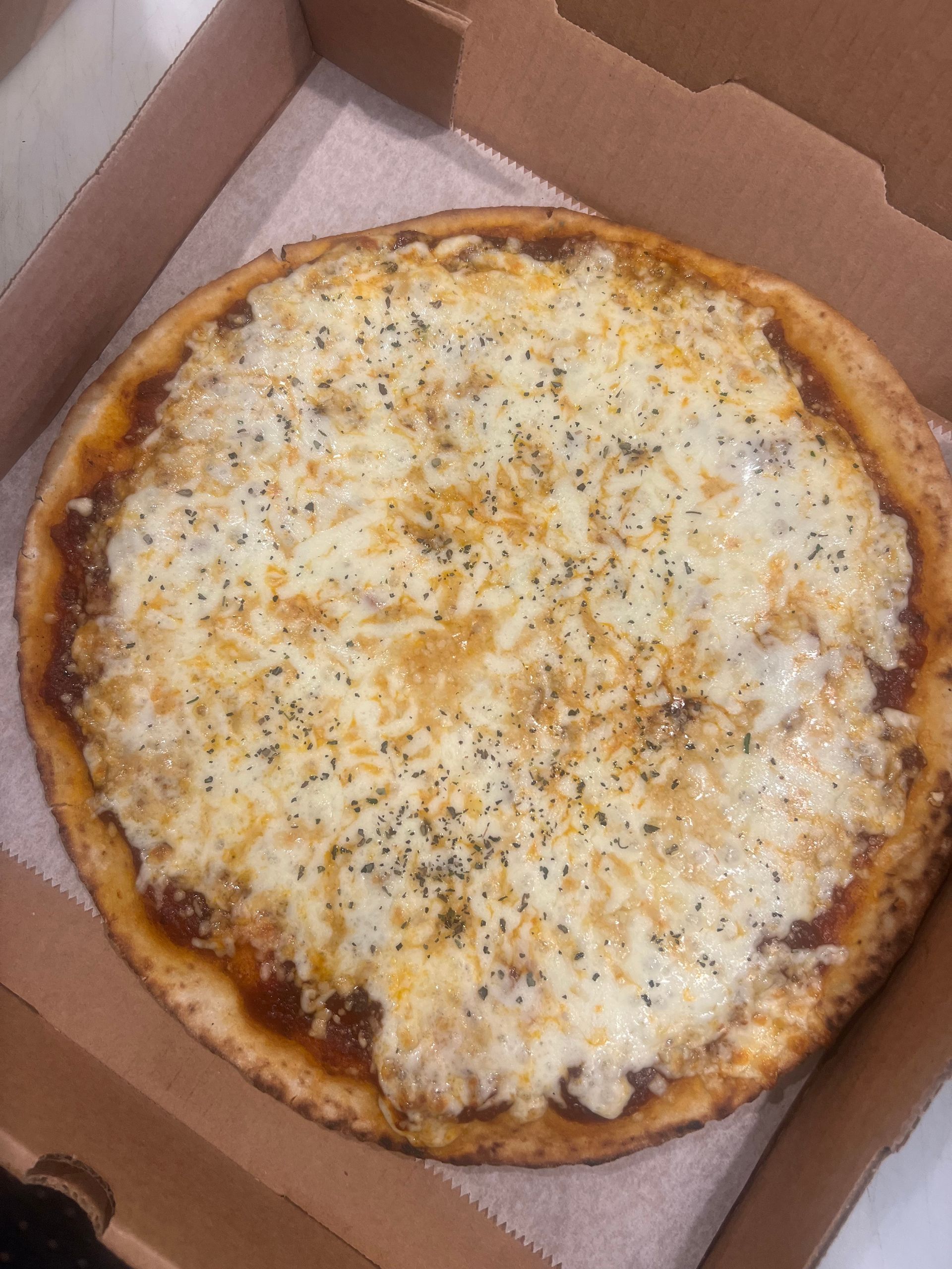 Pizza with cheese and herbs in a cardboard box.