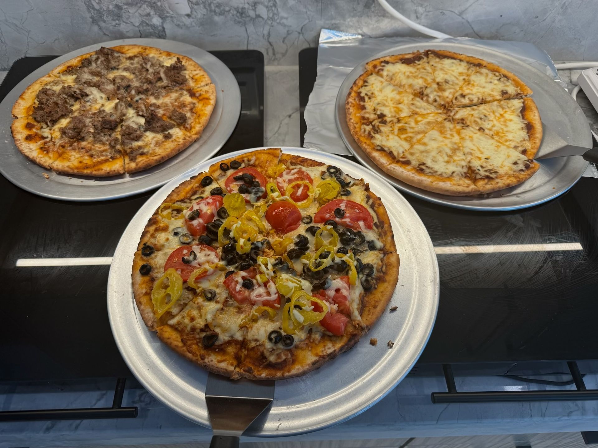 Three pizzas on metal trays: one with meat, one with cheese, and one with vegetables.