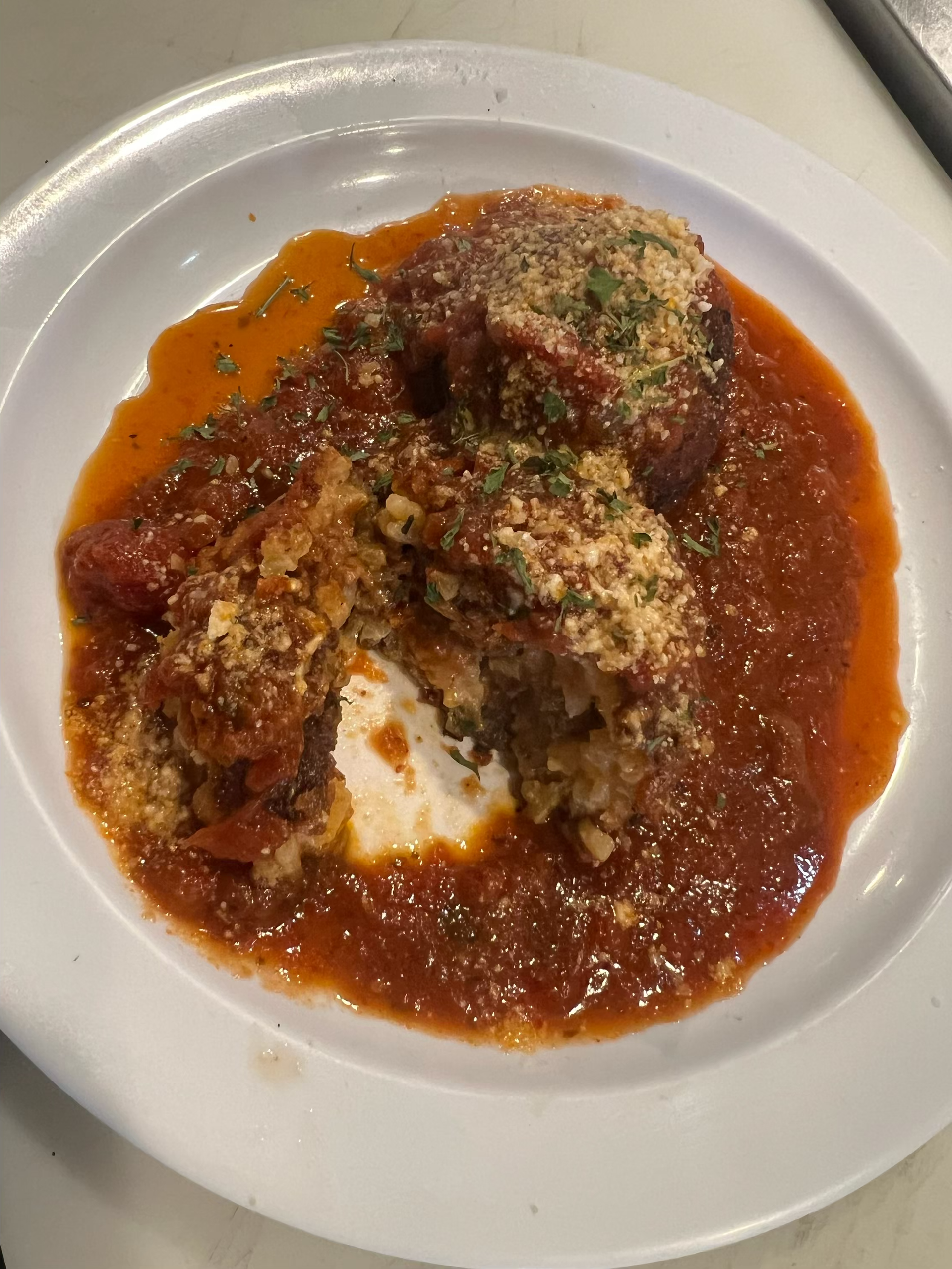 Meatballs in tomato sauce, sprinkled with grated cheese, on a white plate.