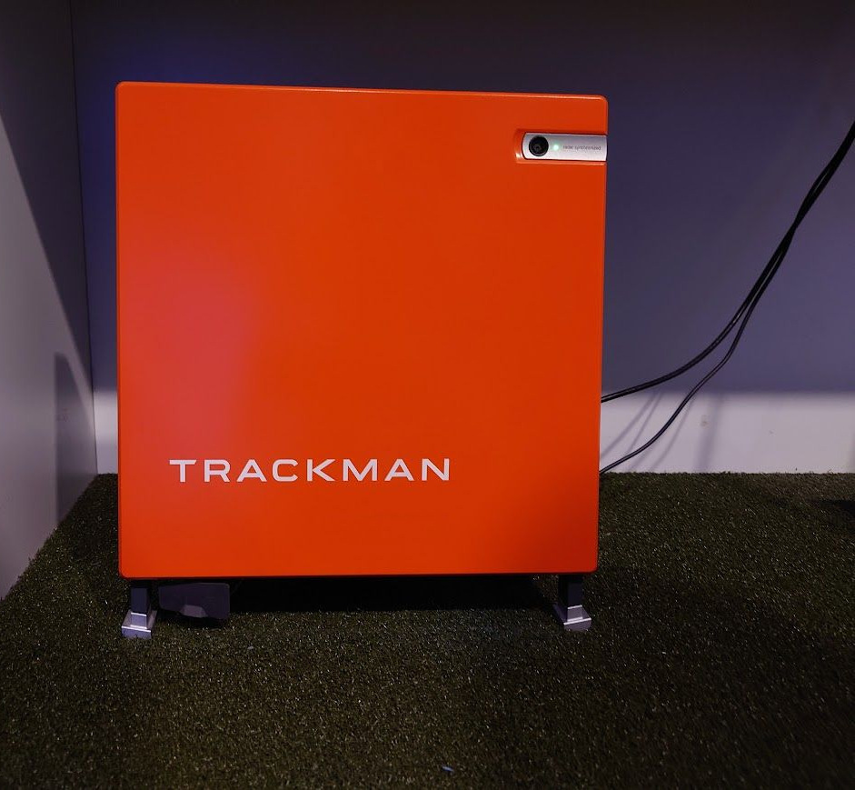 Een man met een hoed zwaait met een golfclub op een zonnige, groene golfbaan.