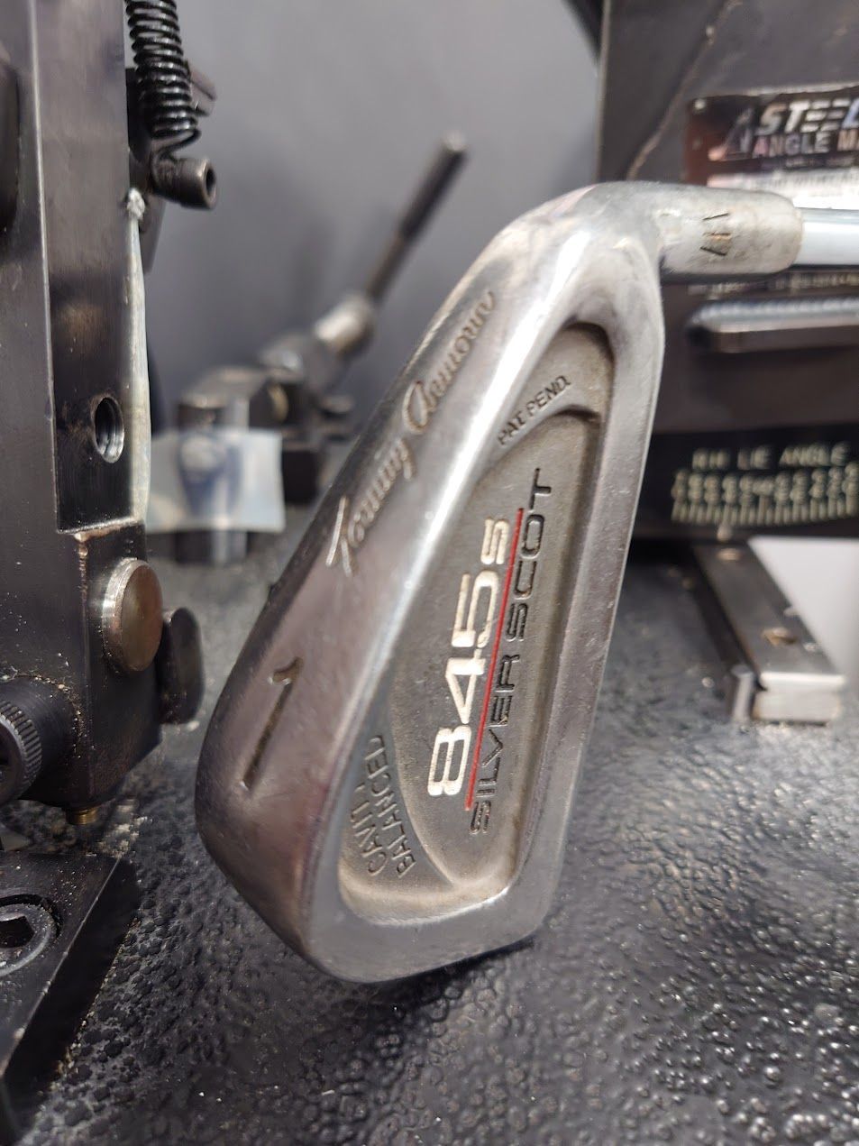 Een jong kind lacht terwijl het een golfclub vasthoudt op een groene golfbaan; mensen op de achtergrond.