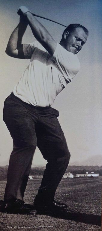 Vrouw in golfkleding op een groene golfbaan, met een golfclub en golftas in haar handen, kijkt weg.