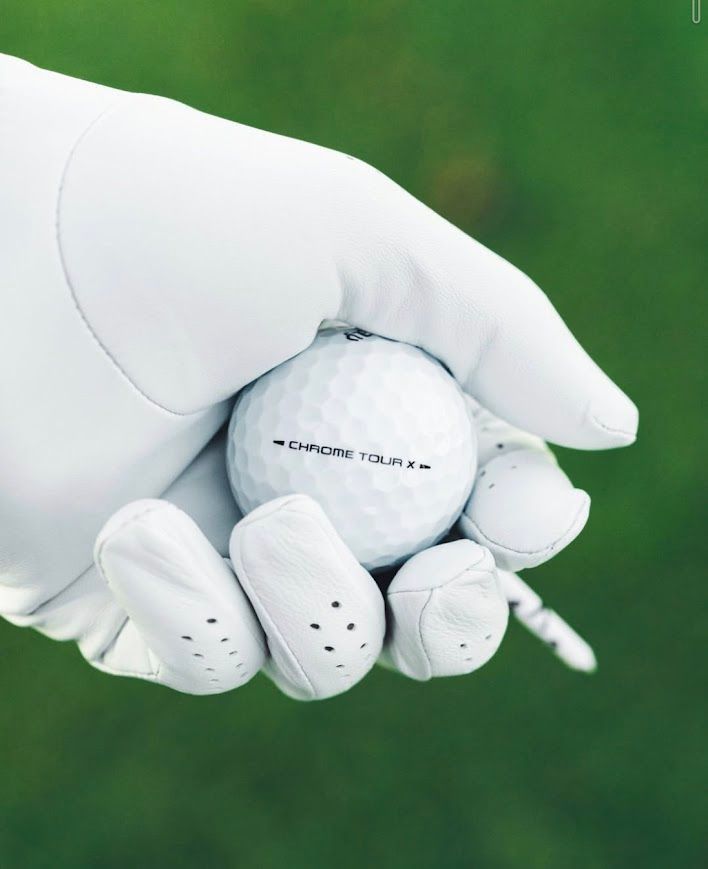 Een jong kind lacht terwijl het een golfclub vasthoudt op een groene golfbaan; mensen op de achtergrond.