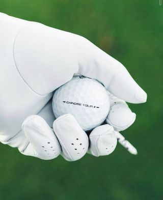 Een jong kind lacht terwijl het een golfclub vasthoudt op een groene golfbaan; mensen op de achtergrond.