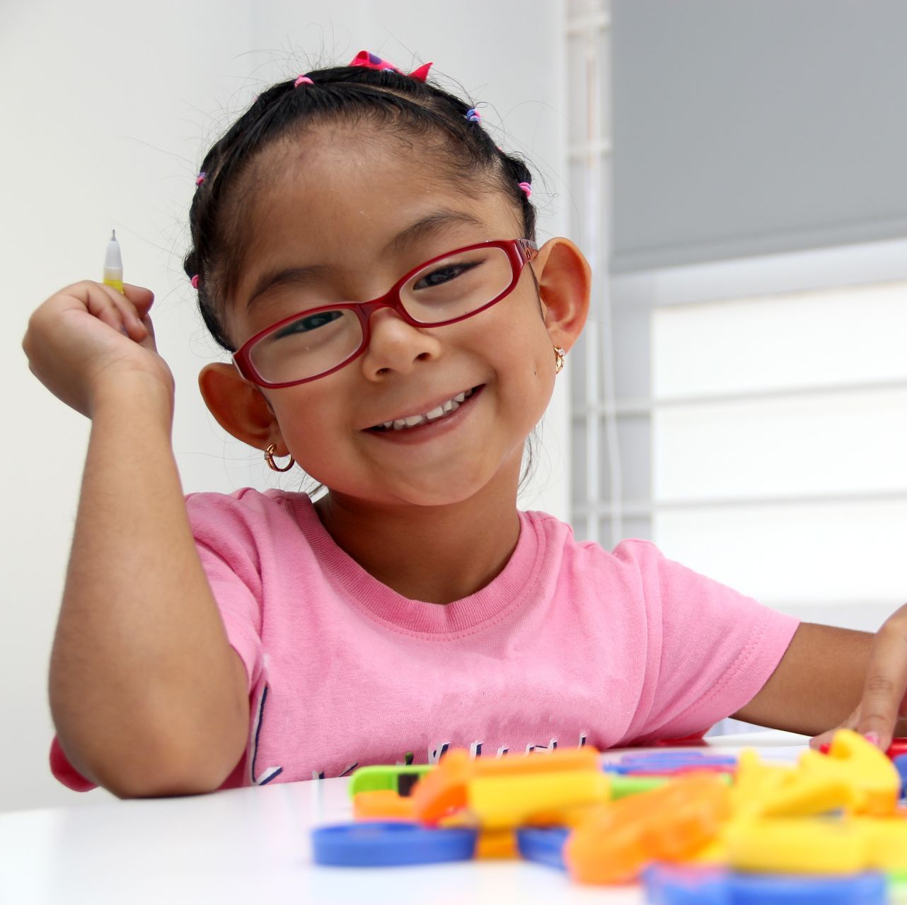 A little girl wearing glasses and a pink shirt is smiling