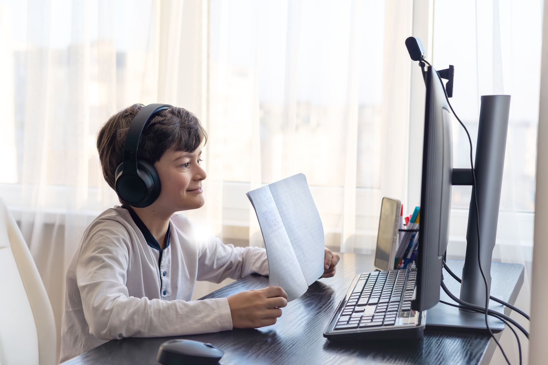 A young boy wearing headphones is sitting at a desk in front of a computer.