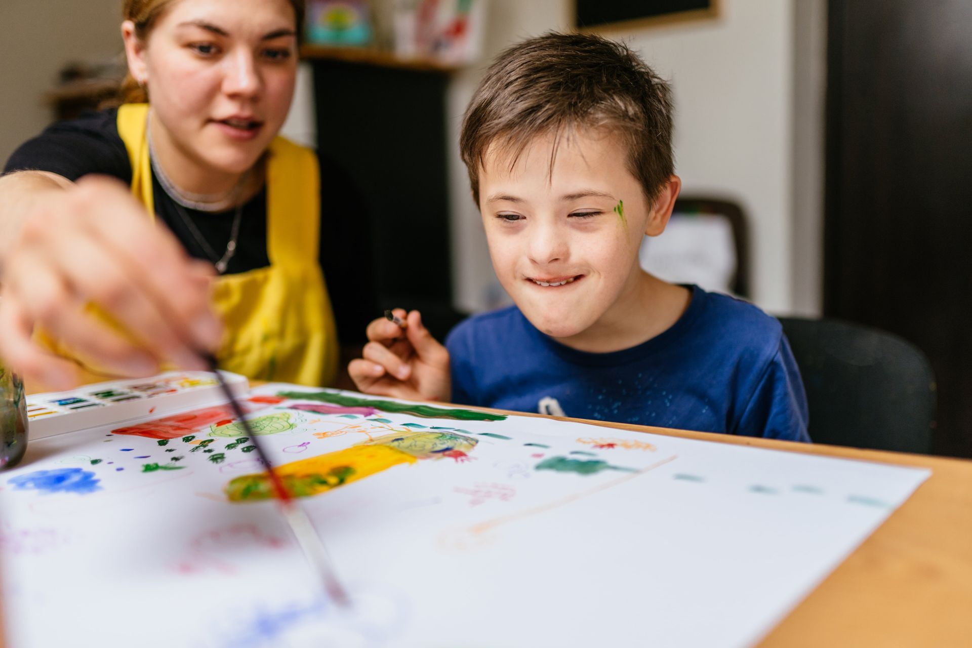 A young boy with down syndrome is sitting at a table playing with colorful toys.