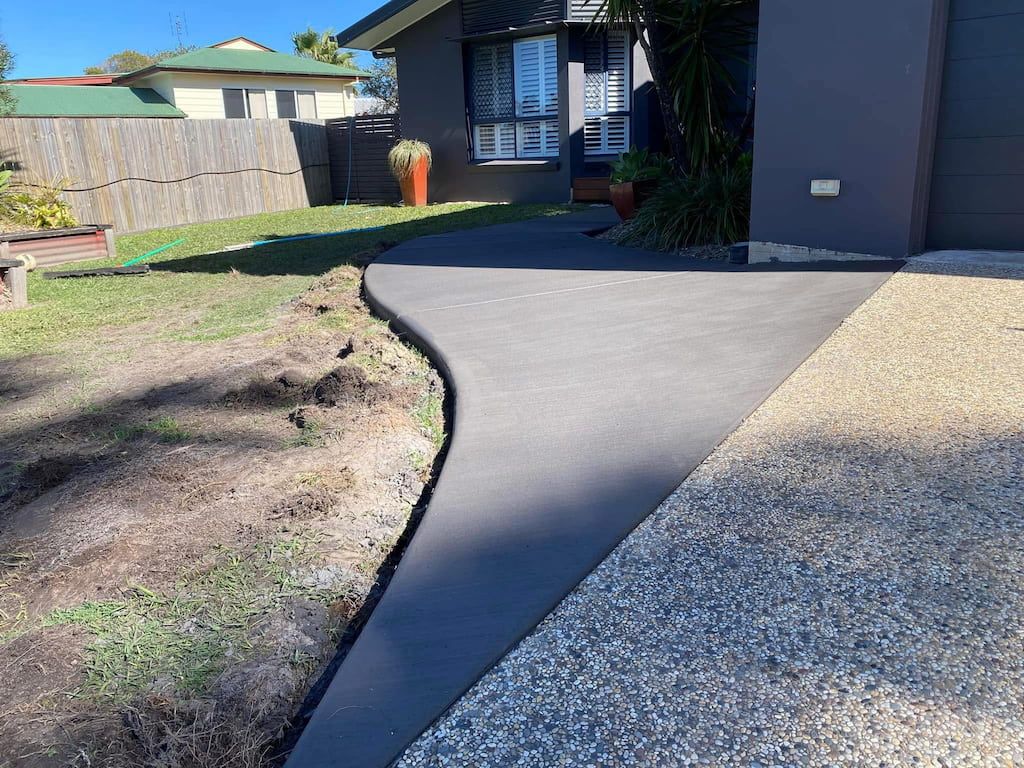 A concrete walkway leading to a house with a fence in the background.