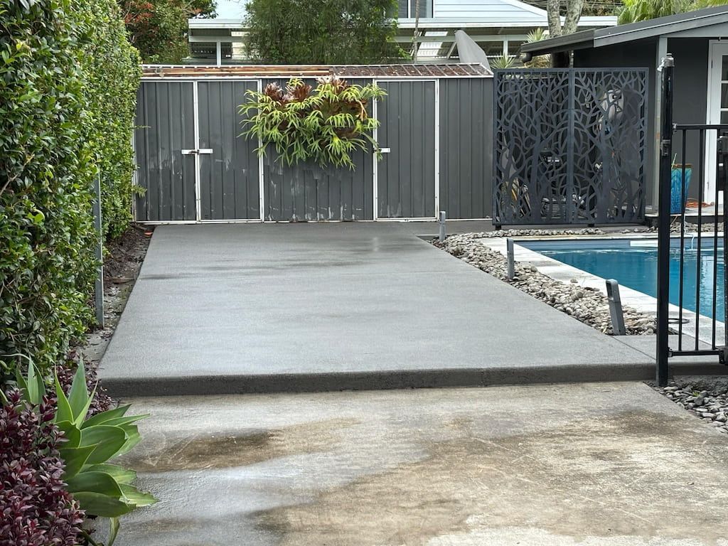 A concrete driveway leading to a pool with a fence in the background