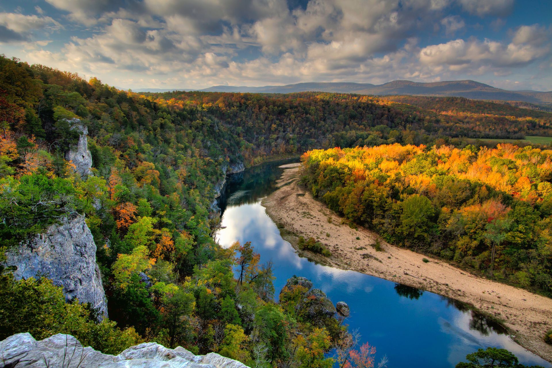 River cutting through a forested canyon with vibrant fall colors and cloudy sky.