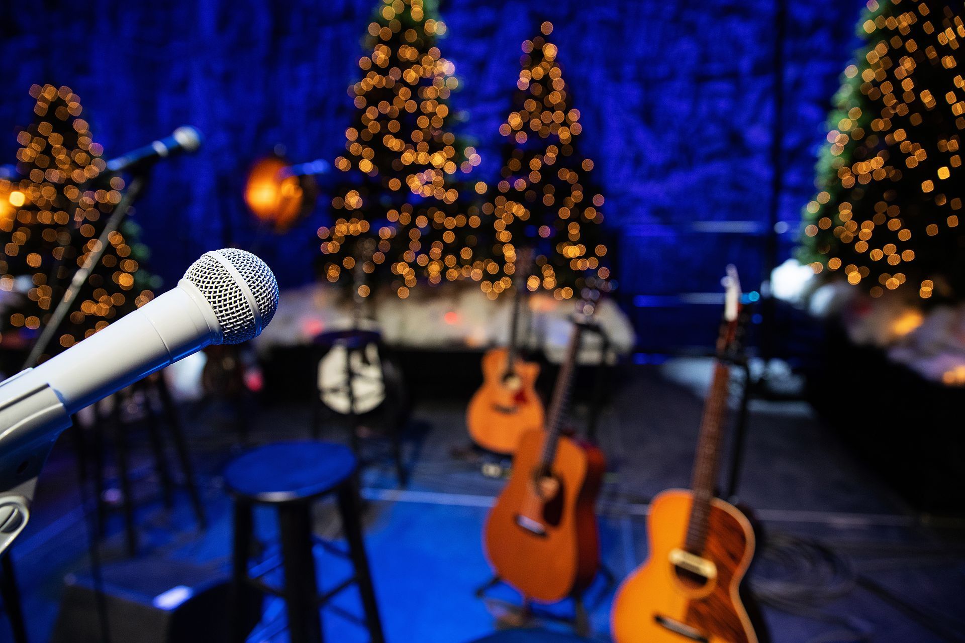 A microphone is on a stage with guitars and christmas trees in the background