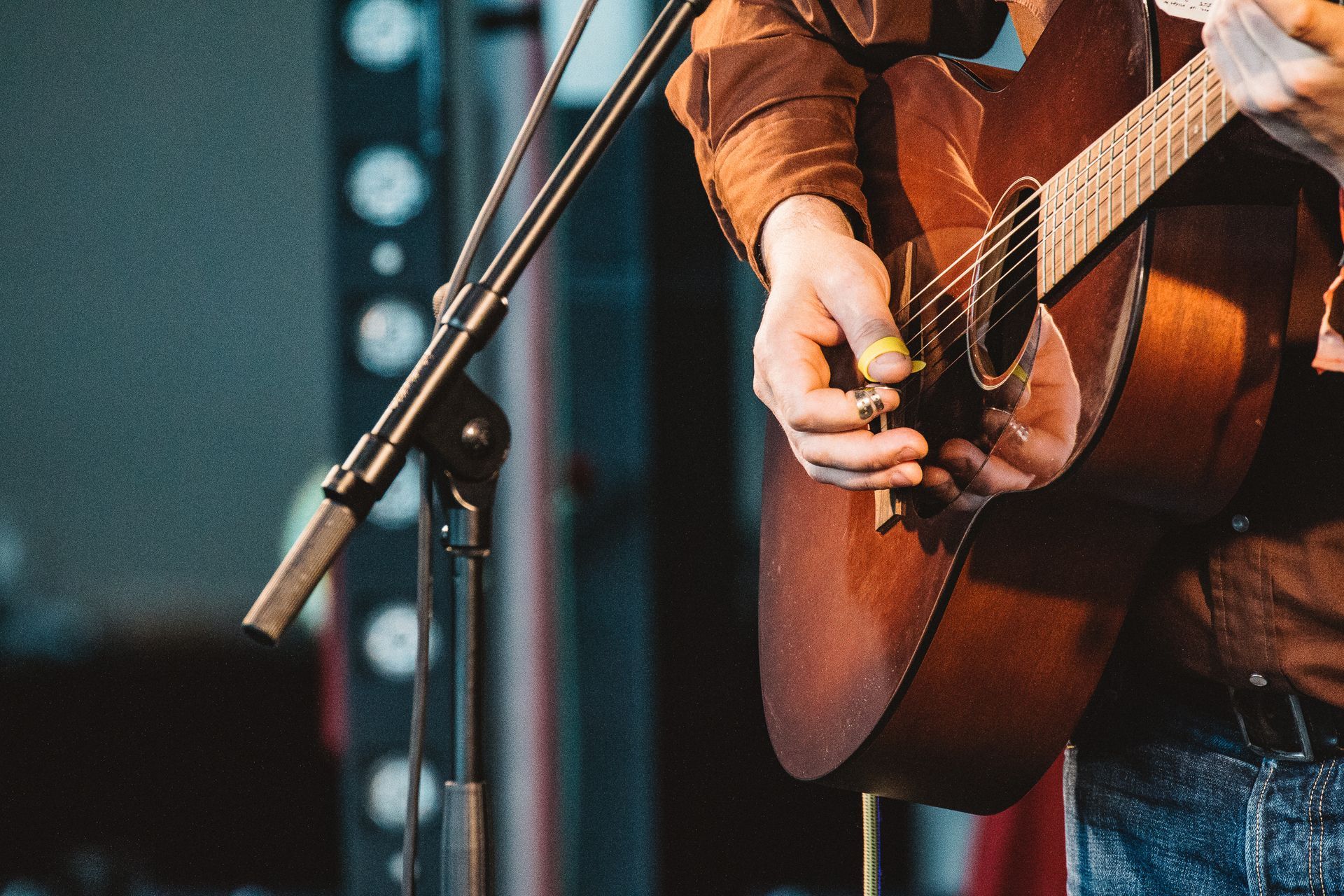 A man is playing an acoustic guitar in front of a microphone.