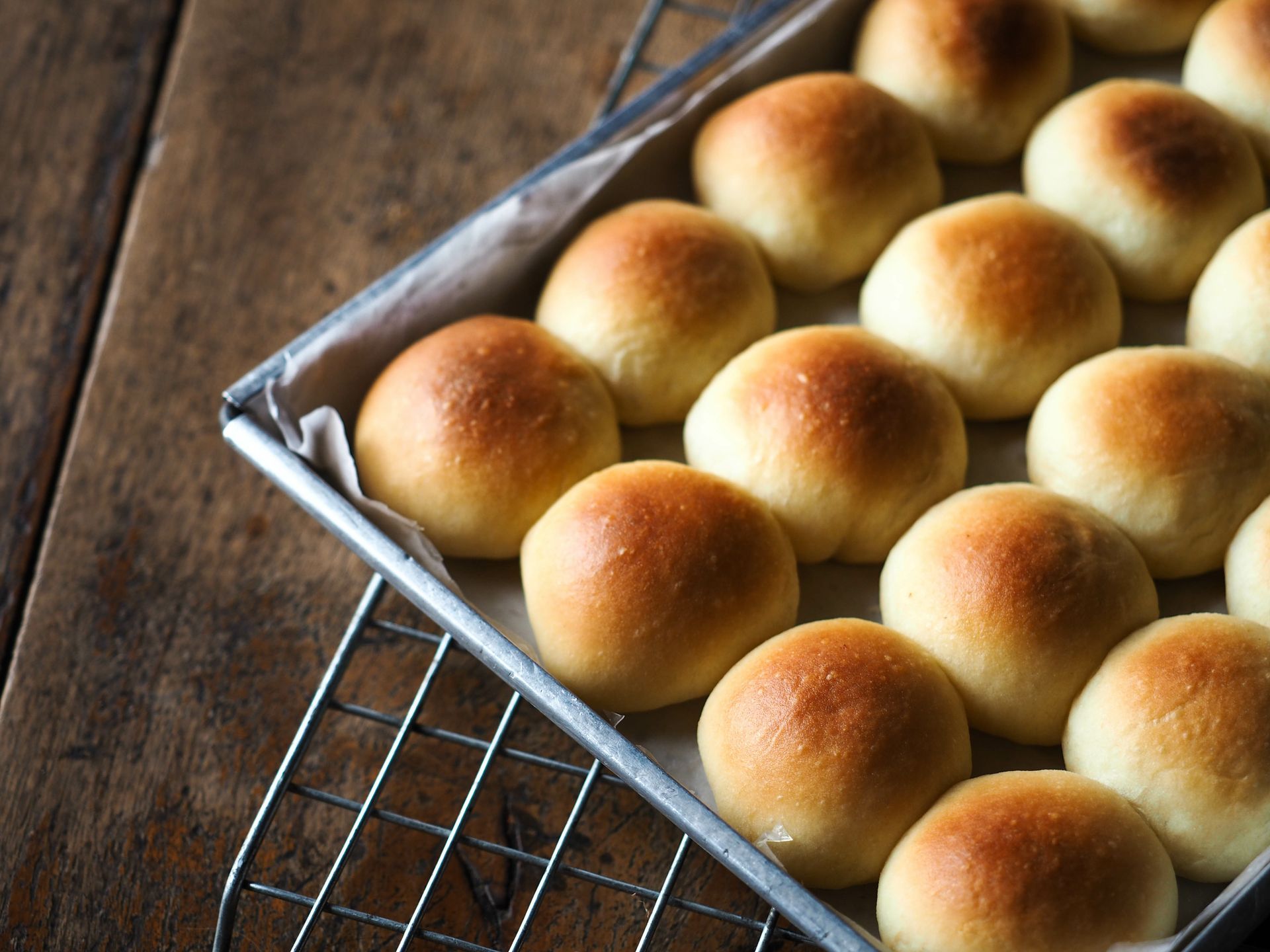 A bunch of rolls are sitting on a wire rack on a wooden table.
