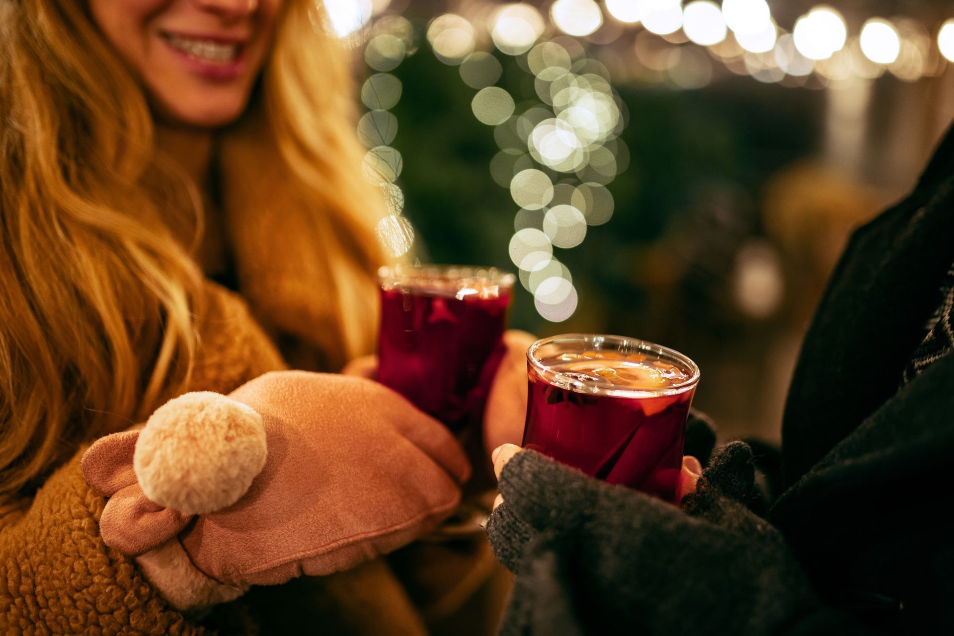 People toasting with glasses of mulled wine, festive lights in background.