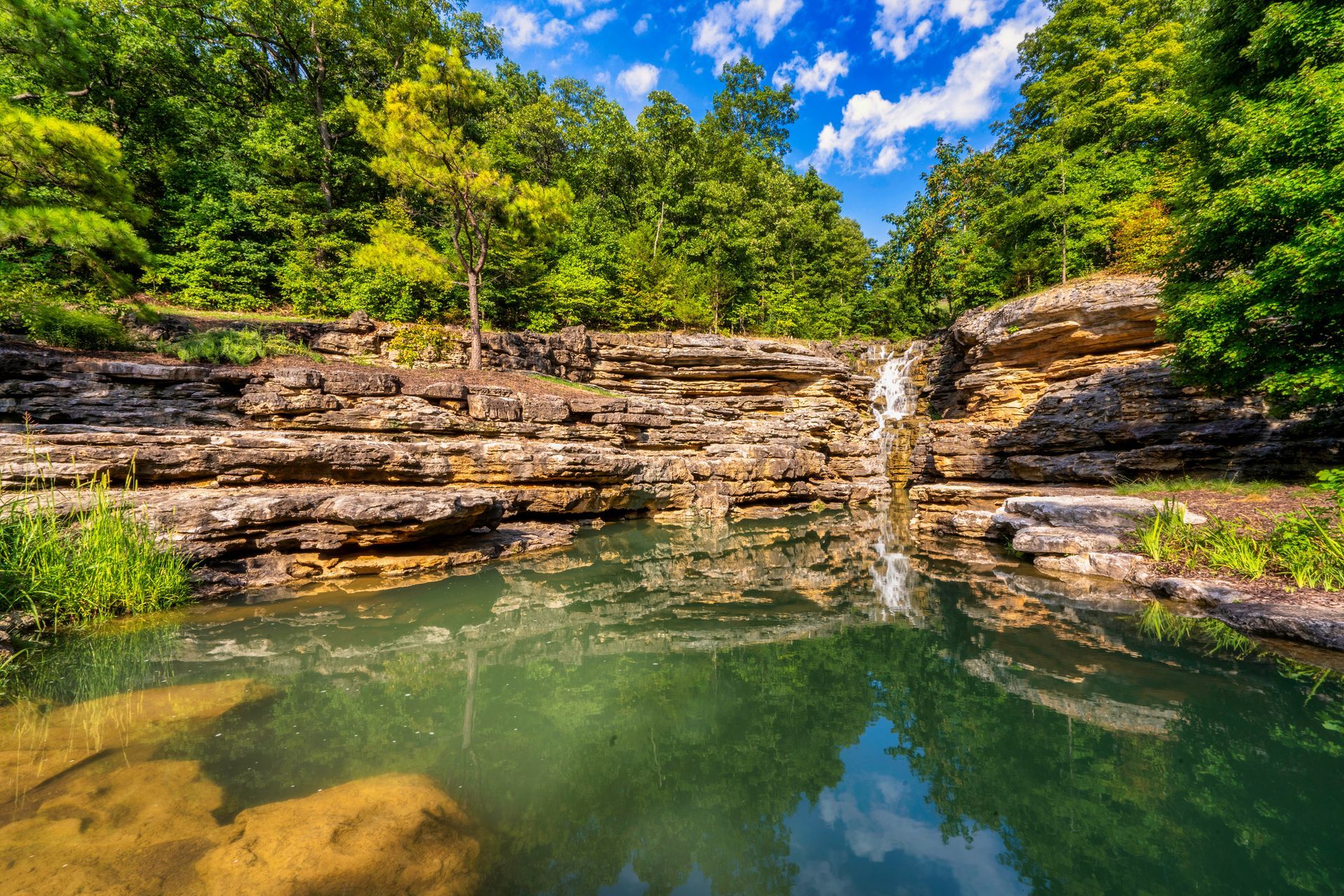 There is a waterfall in the middle of a lake surrounded by trees.