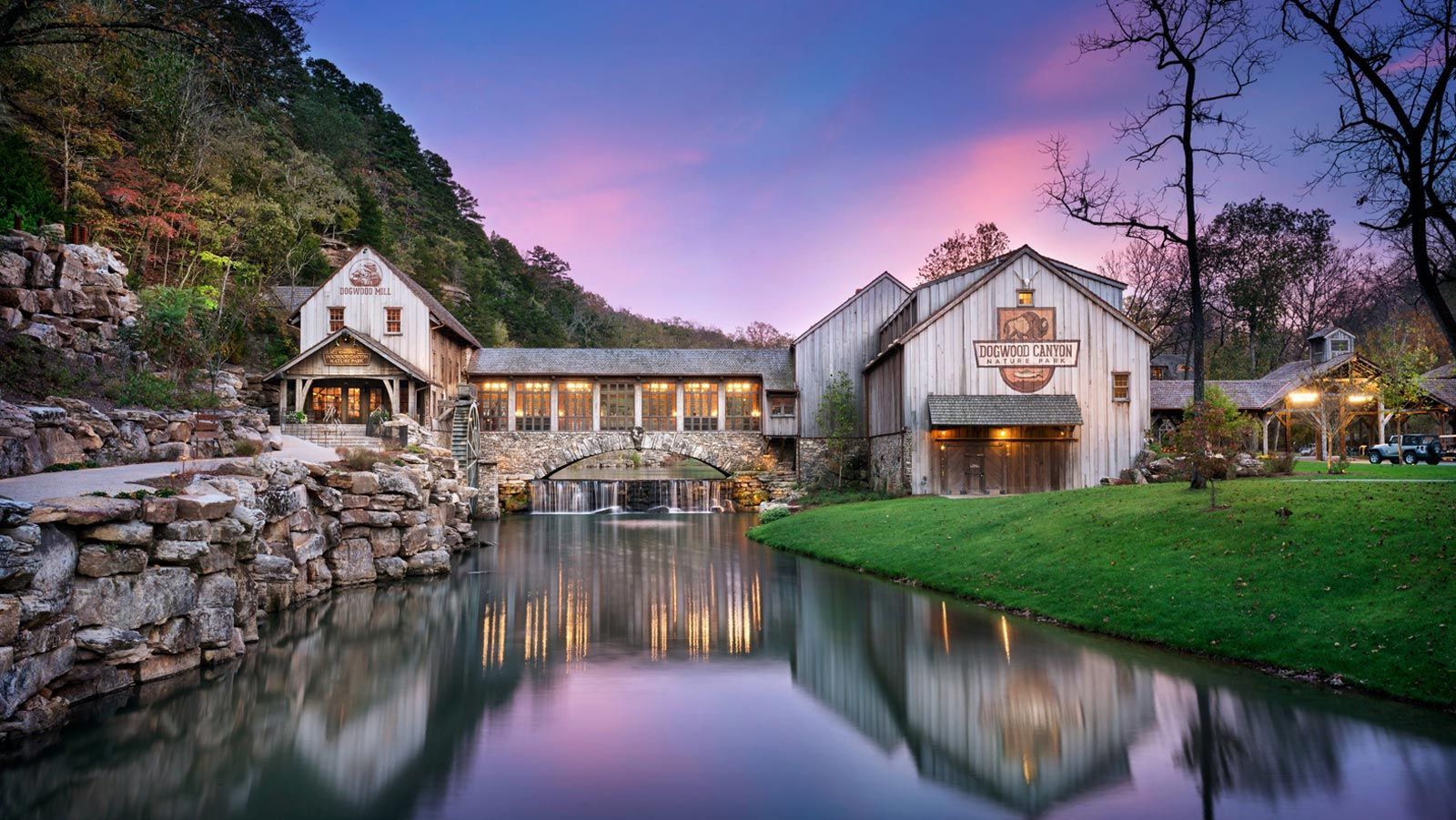 Scenic view of a covered bridge over a calm river, buildings on either side, sunset colors reflected in the water.