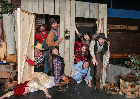 A group of people are posing for a picture in front of a wooden building.