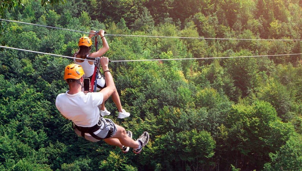 A man and a woman are flying through the air on a zip line.