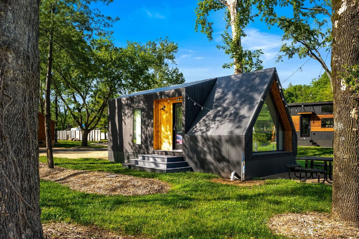 A small house is sitting in the middle of a lush green field surrounded by trees.