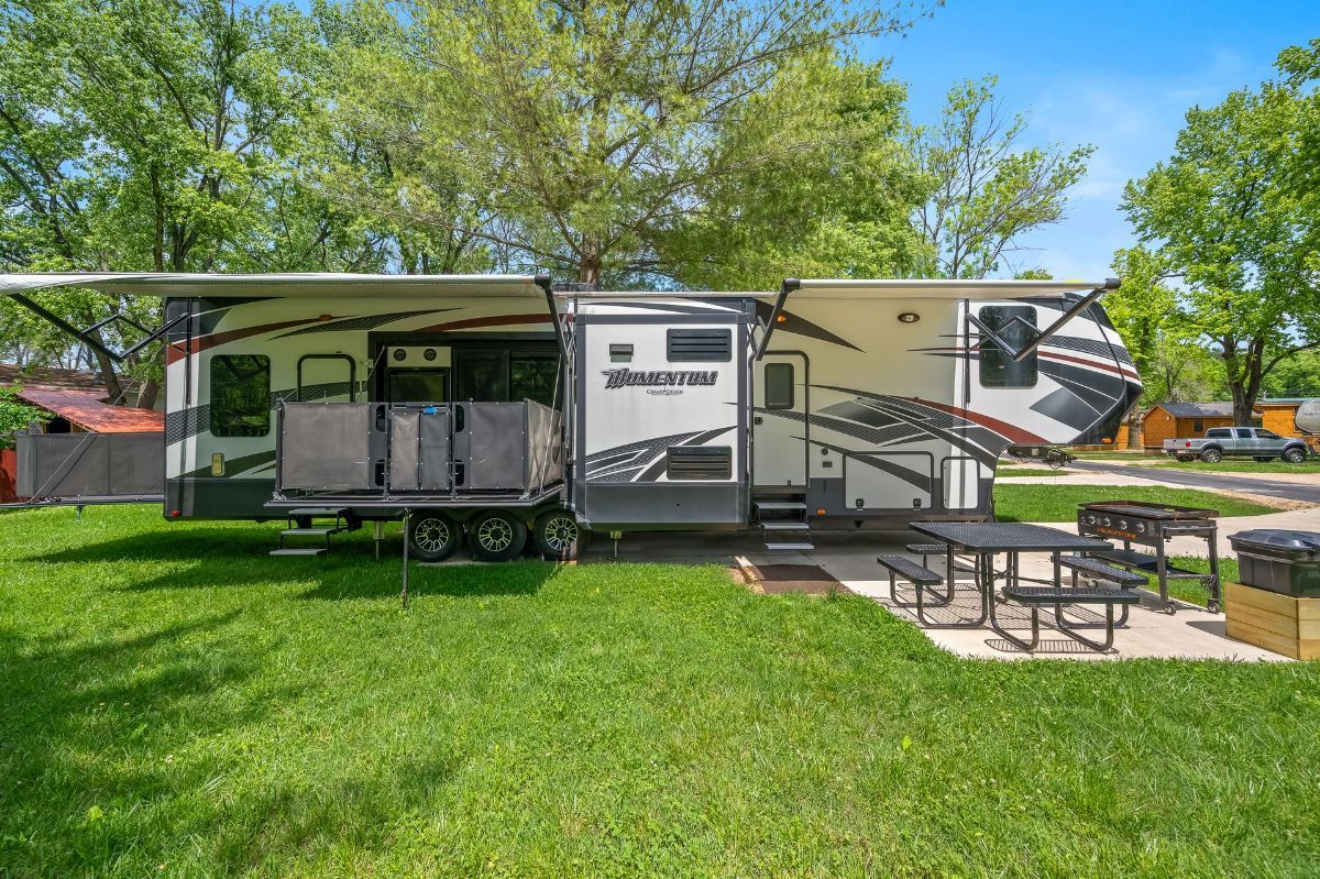 A rv is parked in a grassy field with a picnic table and chairs.