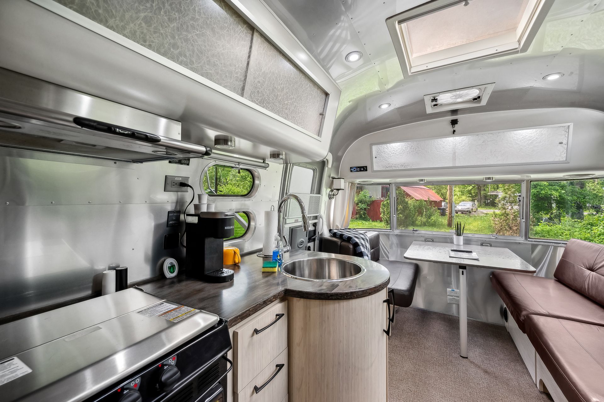Interior of an Airstream trailer with a kitchen, dining area, and windows overlooking trees.
