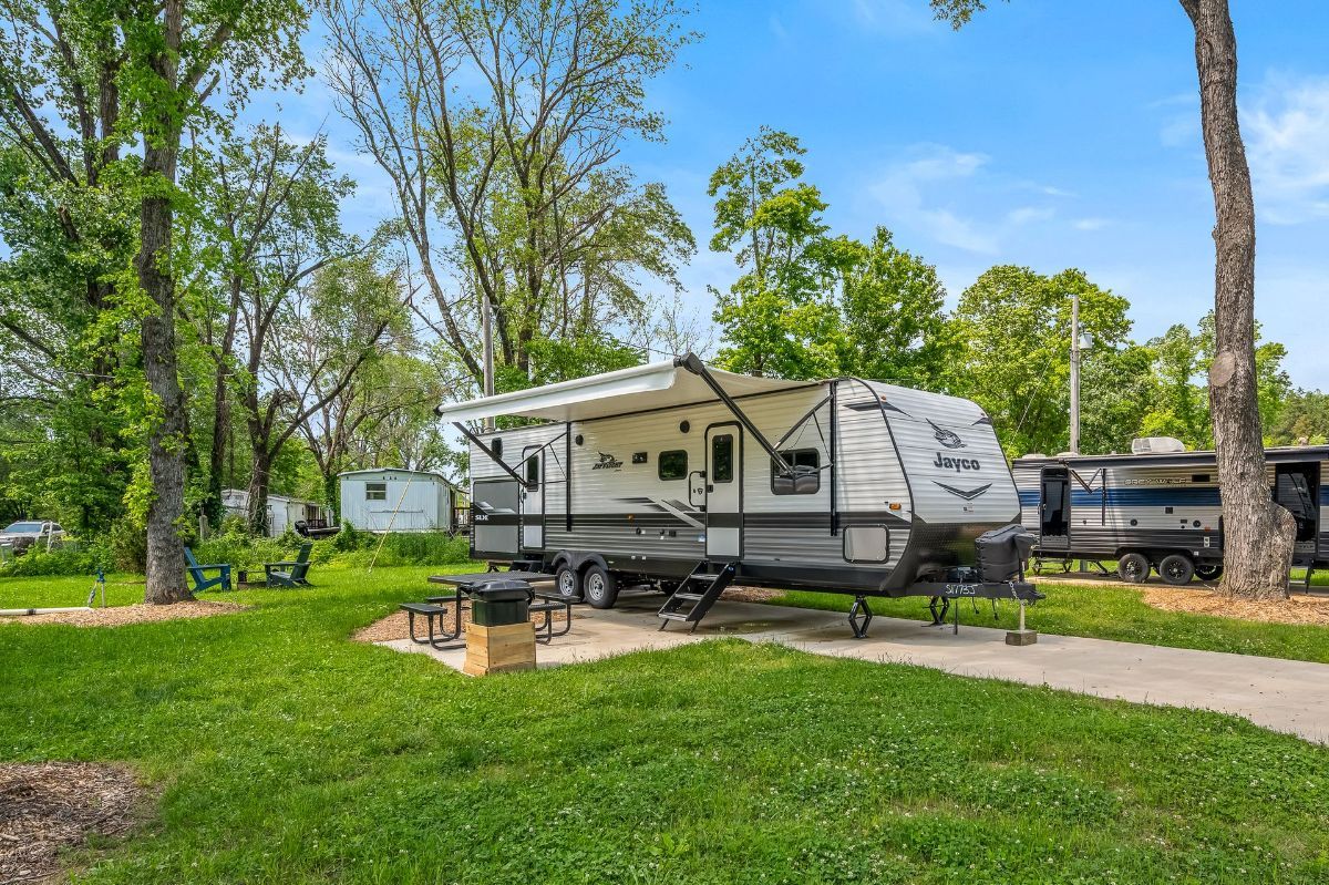 A rv is parked in a grassy area next to trees.