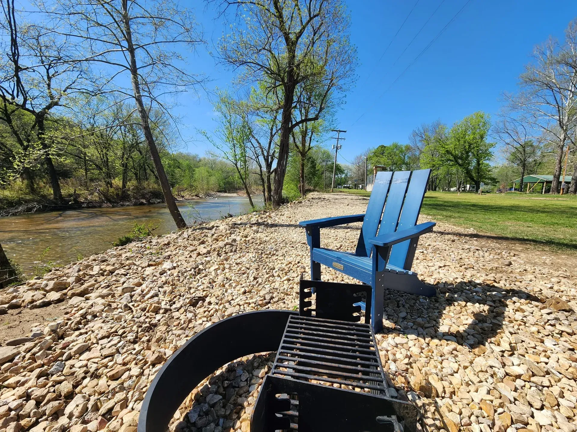 A blue chair is sitting next to a fire pit on the shore of a river.