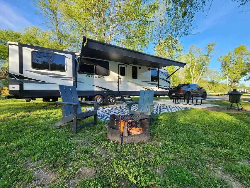 A rv is parked in a grassy field next to a fire pit.