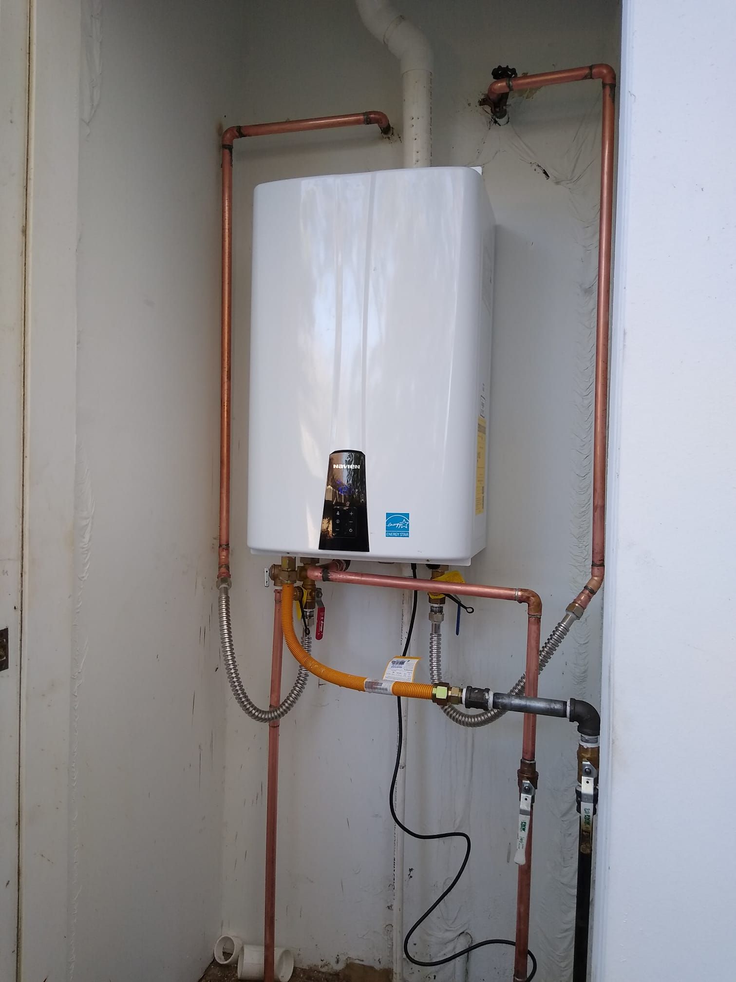 White tankless water heater with copper pipes in a utility room.