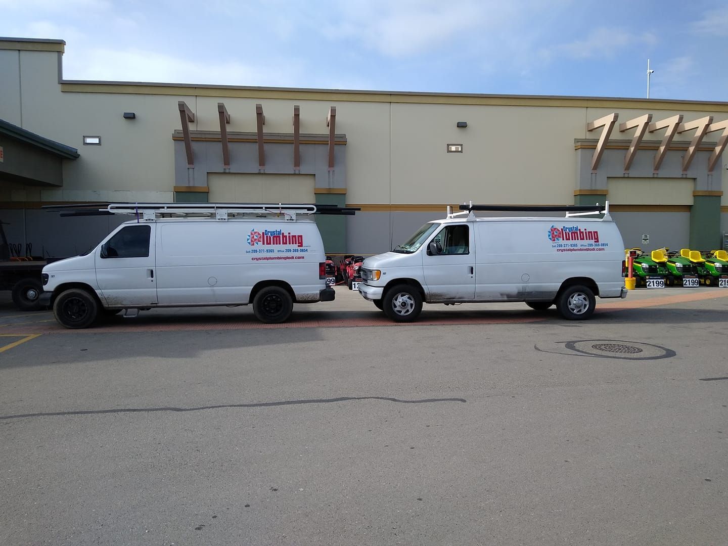 Two white service vans parked in front of a building. Both have ladder racks and company logos.