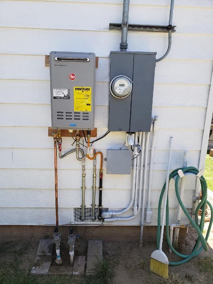 Exterior view of a wall-mounted water heater and electrical panel against white siding. Copper and gray components.