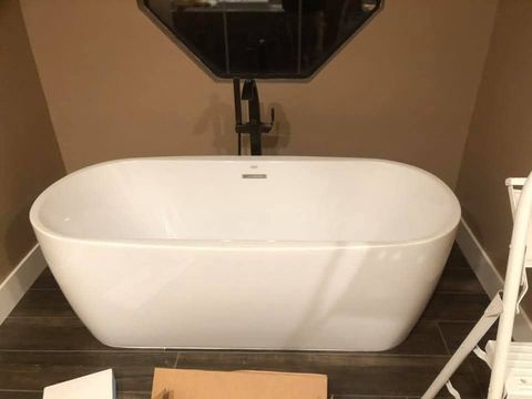 Freestanding white bathtub in a bathroom with dark floors, beige walls, and a black faucet.