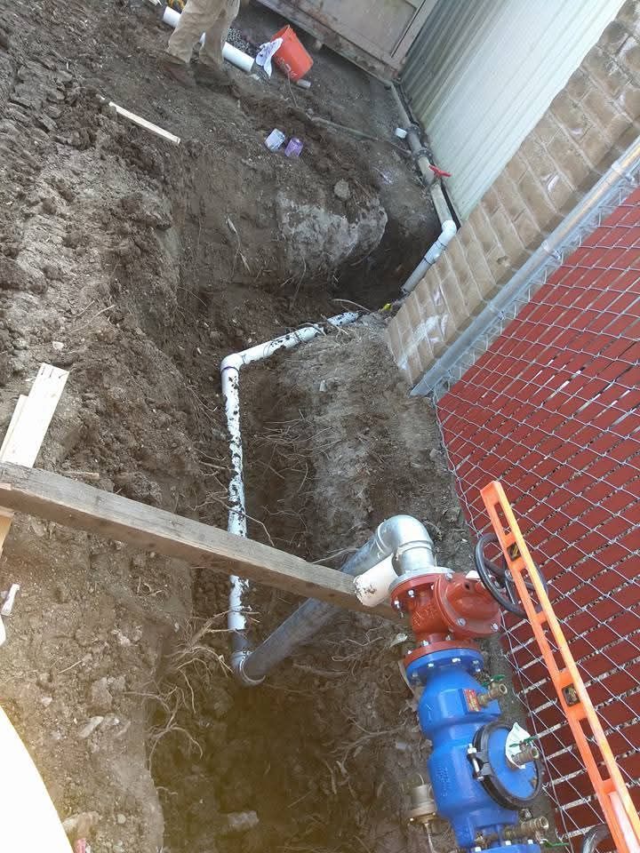 Pipes laid in a trench next to a brick wall and a water main, during construction.