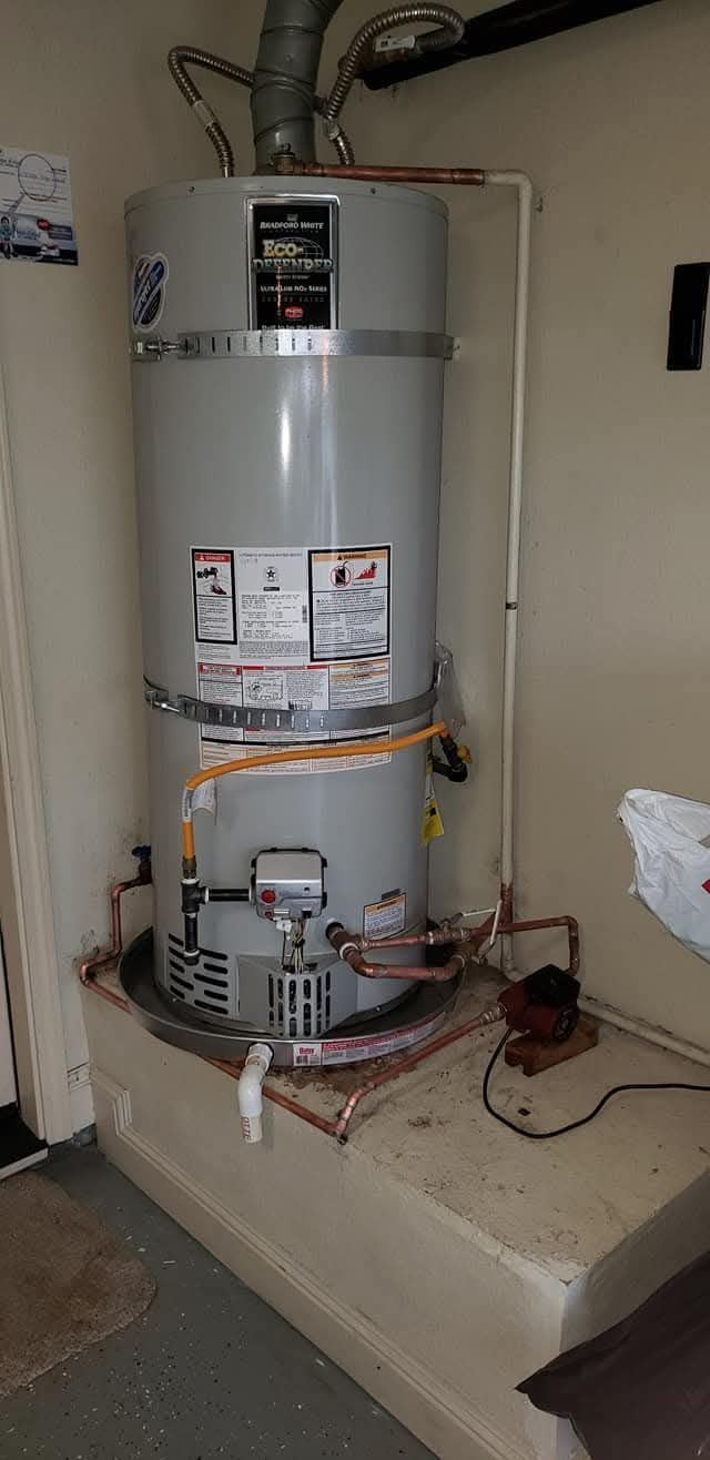 A water heater is installed in a room. The heater is cylindrical and gray, with visible piping.